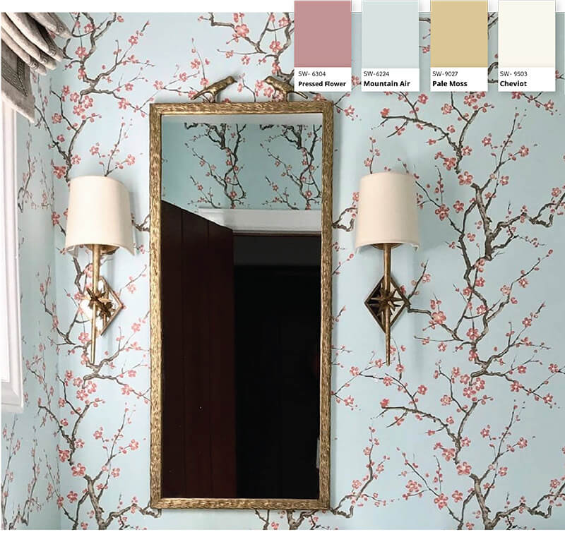 A bathroom with light teal wallpaper covered in pink cherry blossoms accompanied by a gold mirror